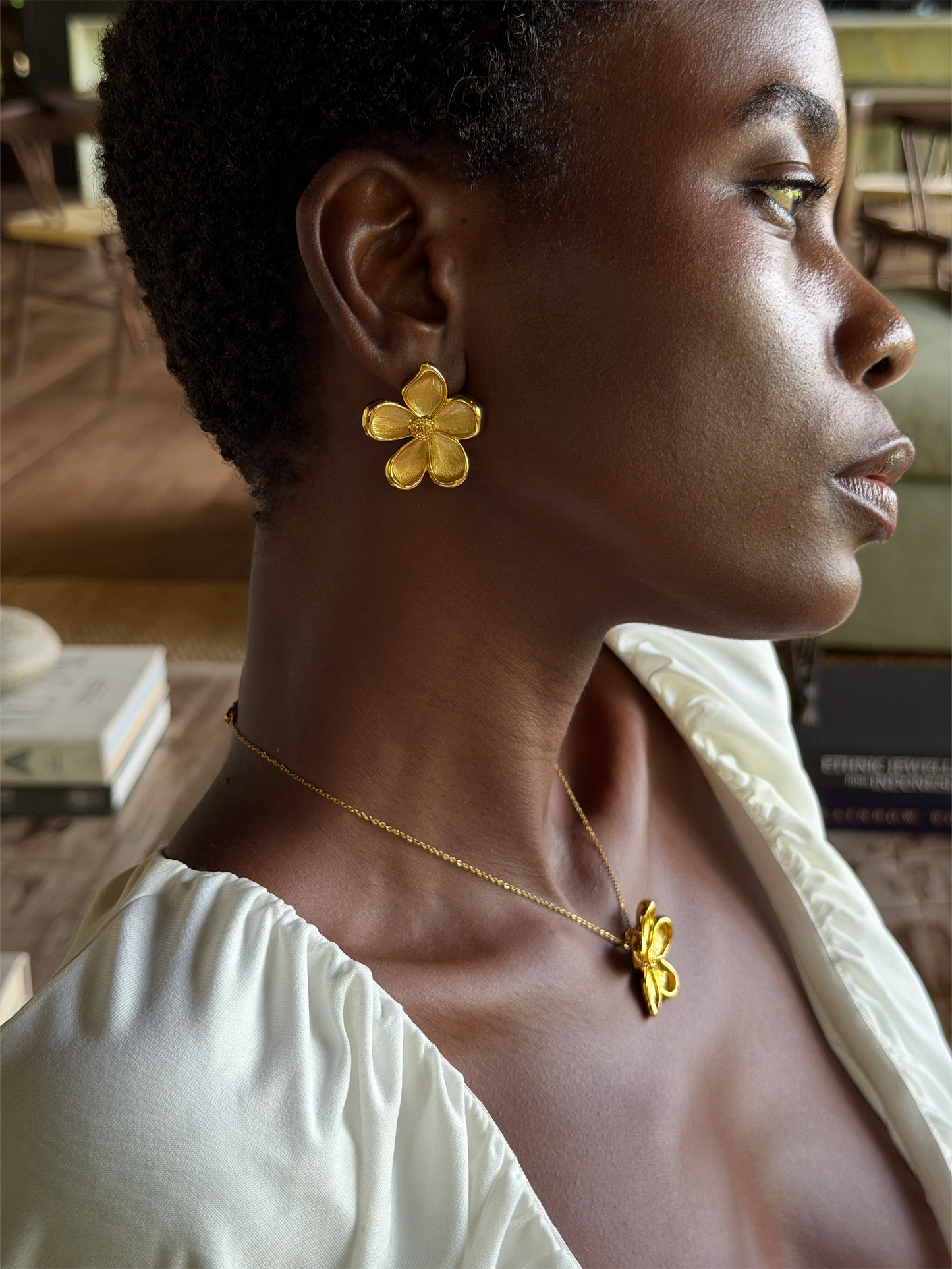 Woman wearing statement golden flower earrings and a necklace in an indoor setting