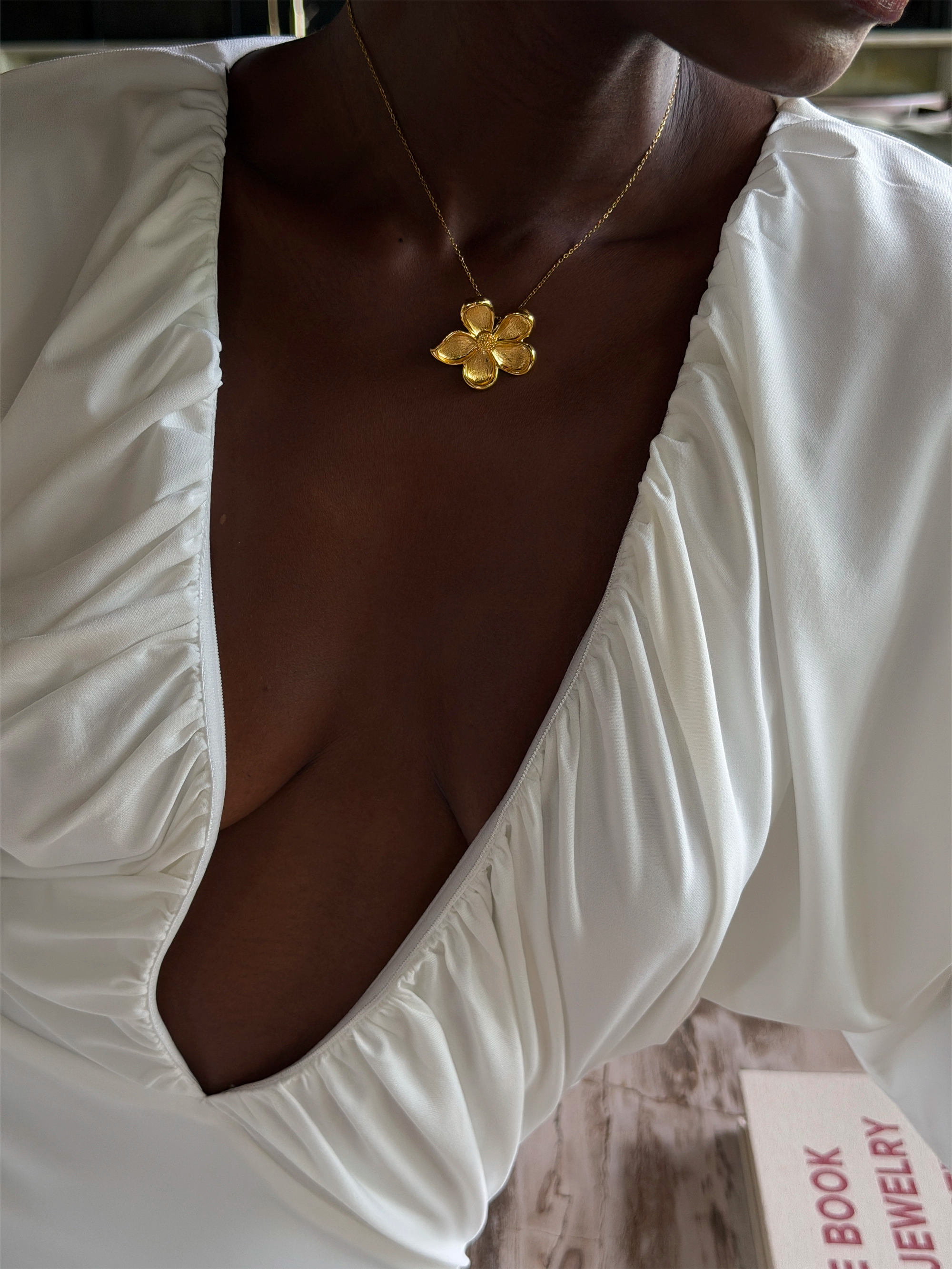 Gold necklace with a floral pendant worn with a deep v neckline dress.