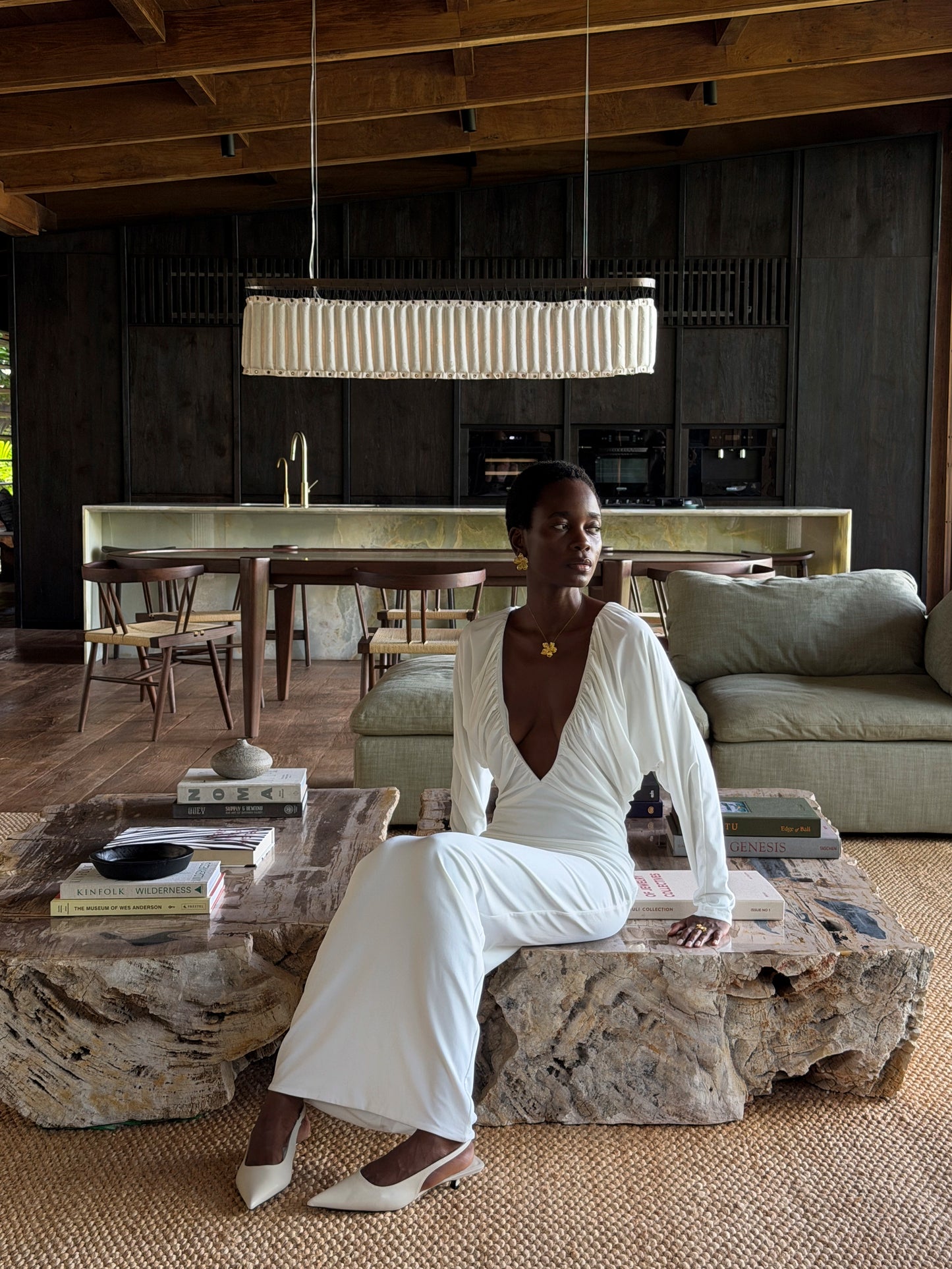 Woman in a white outfit sitting on a stone bench in a modern interior setting wearing maxi flower necklace and maxi flower earrings.
